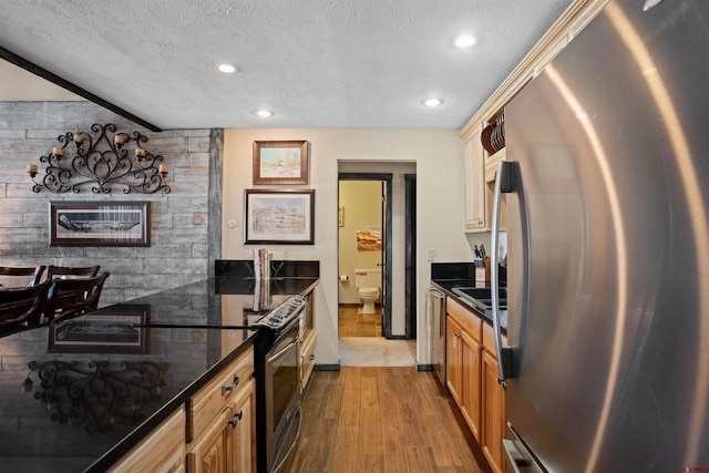 kitchen featuring dark stone counters, a textured ceiling, stainless steel appliances, and hardwood / wood-style flooring