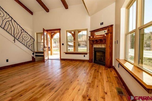 unfurnished living room featuring beamed ceiling, wood-type flooring, and a healthy amount of sunlight