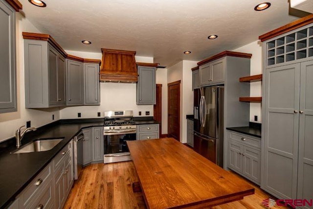 kitchen with custom exhaust hood, stainless steel appliances, light wood-type flooring, sink, and gray cabinetry