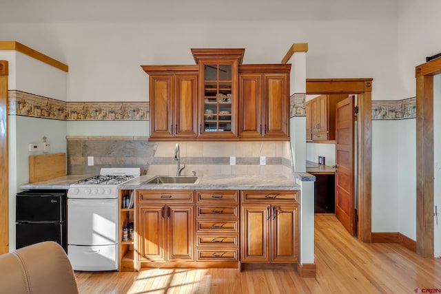 kitchen featuring tasteful backsplash, white gas range oven, light stone countertops, light hardwood / wood-style floors, and sink