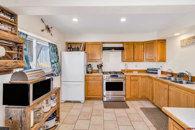 kitchen with light tile patterned floors, stainless steel gas stove, white fridge, and sink