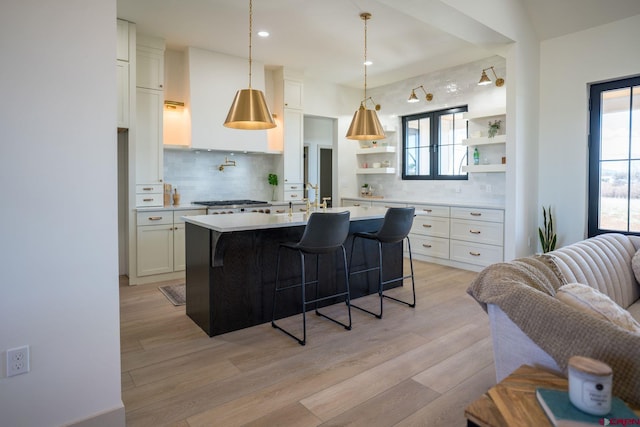 kitchen featuring light hardwood / wood-style flooring, tasteful backsplash, an island with sink, and white cabinetry