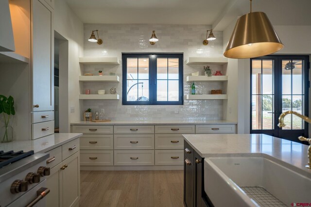 kitchen with light hardwood / wood-style flooring, tasteful backsplash, sink, french doors, and white cabinetry