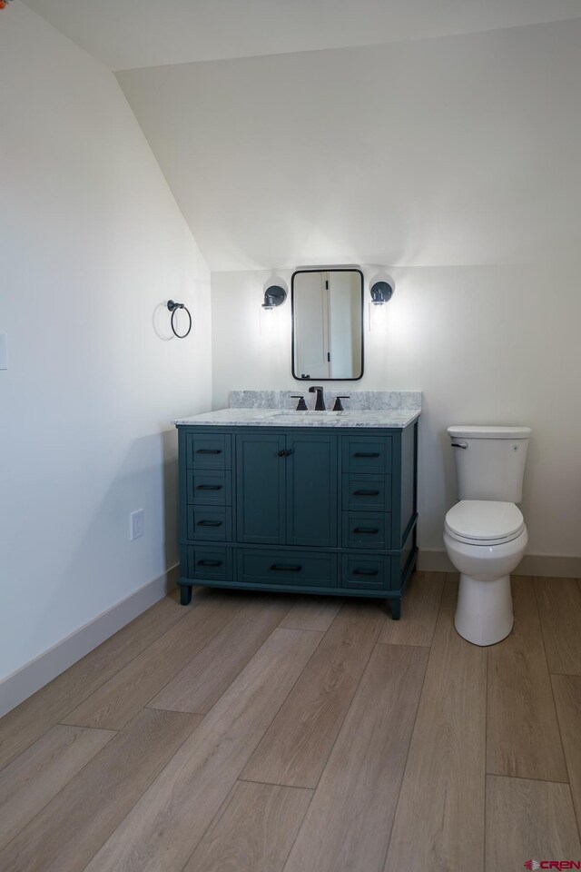 bathroom with wood-type flooring, vaulted ceiling, toilet, and vanity