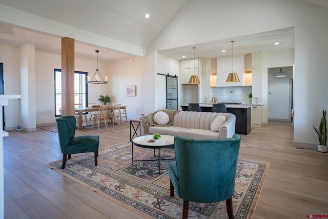 living room with high vaulted ceiling, a barn door, a notable chandelier, and light hardwood / wood-style floors