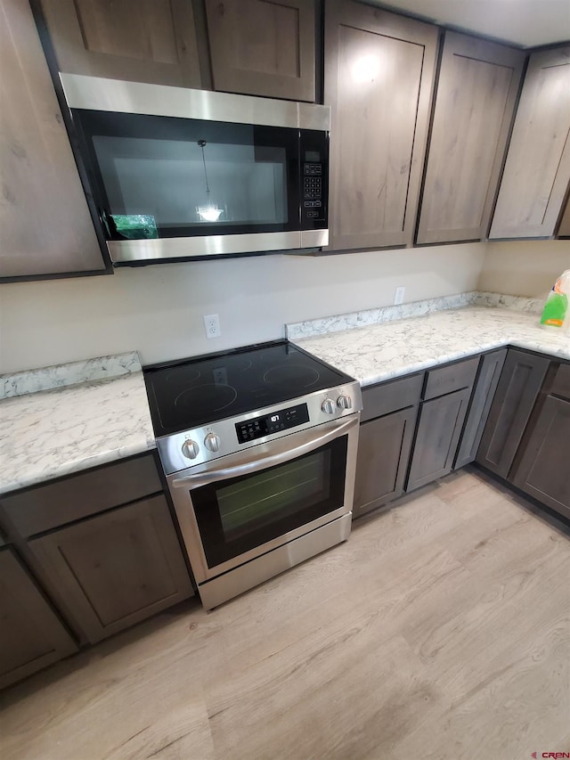 kitchen with light hardwood / wood-style floors, light stone countertops, appliances with stainless steel finishes, and dark brown cabinets