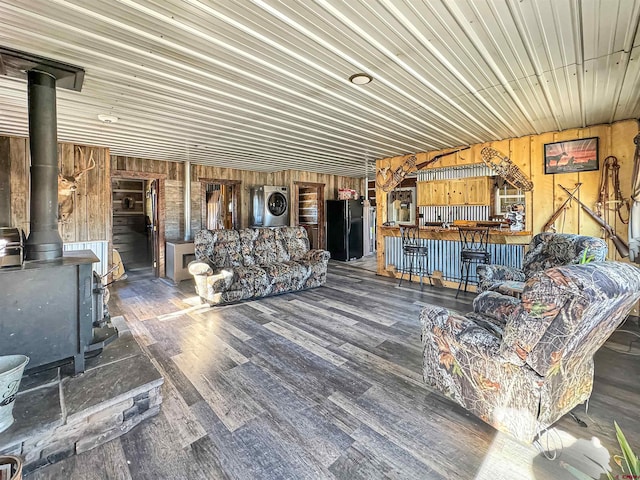 living room with stacked washer and clothes dryer, a wood stove, hardwood / wood-style floors, and wooden walls