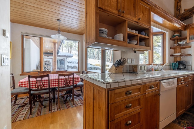 kitchen with sink, white dishwasher, tile countertops, decorative light fixtures, and light wood-type flooring