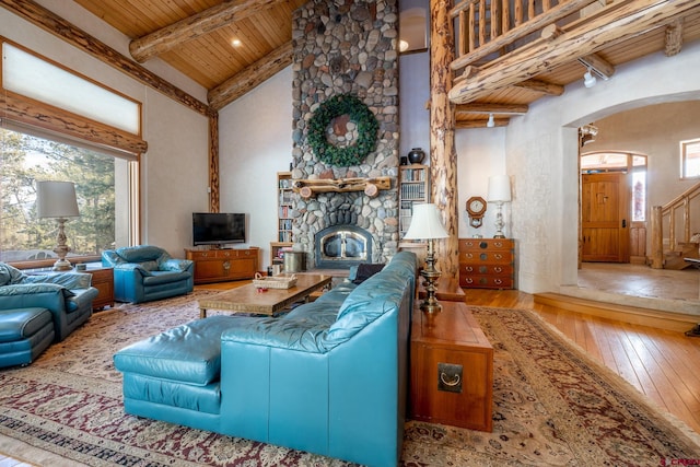 living room featuring beam ceiling, a stone fireplace, high vaulted ceiling, wood ceiling, and light hardwood / wood-style flooring