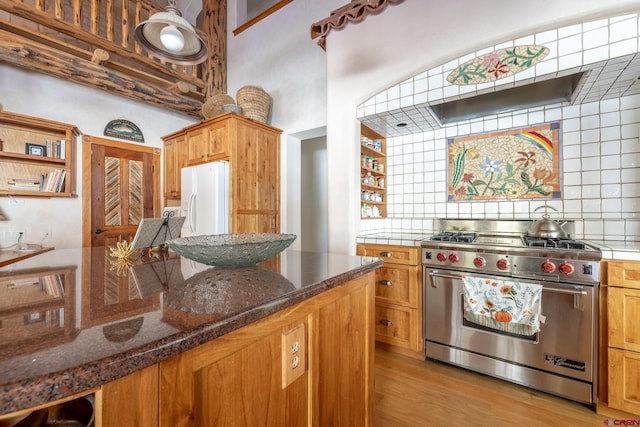 kitchen featuring dark stone counters, backsplash, white refrigerator with ice dispenser, premium stove, and light wood-type flooring