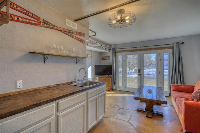 kitchen featuring wood counters, a textured ceiling, sink, white cabinetry, and french doors