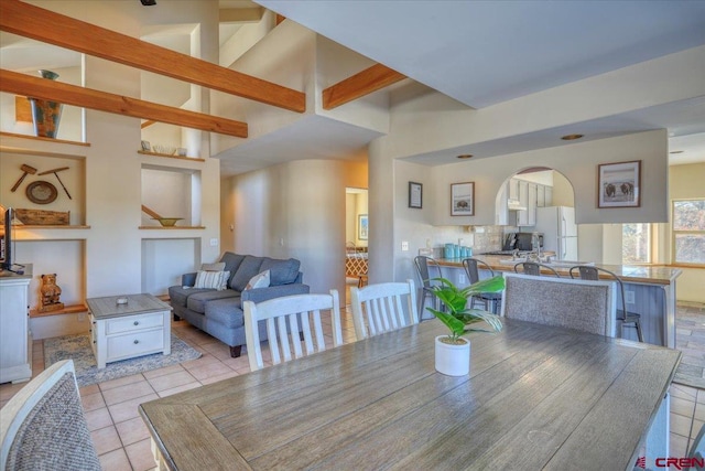 dining space with high vaulted ceiling, light tile flooring, and beamed ceiling