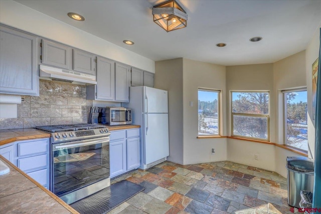 kitchen featuring tasteful backsplash, light tile floors, stainless steel appliances, tile countertops, and extractor fan