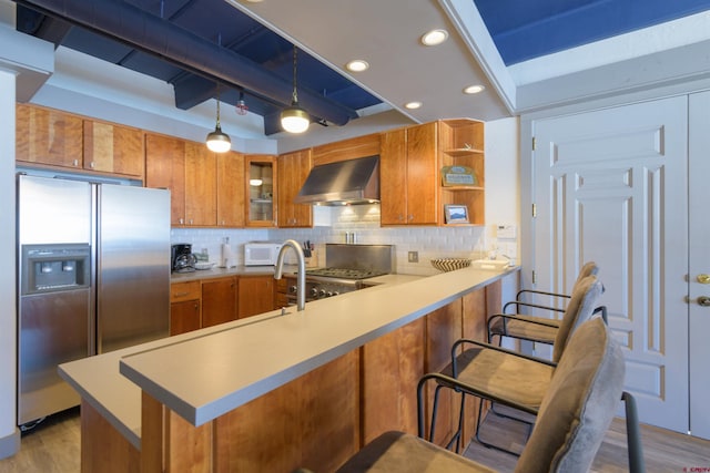 kitchen featuring light hardwood / wood-style flooring, wall chimney range hood, tasteful backsplash, decorative light fixtures, and stainless steel refrigerator with ice dispenser