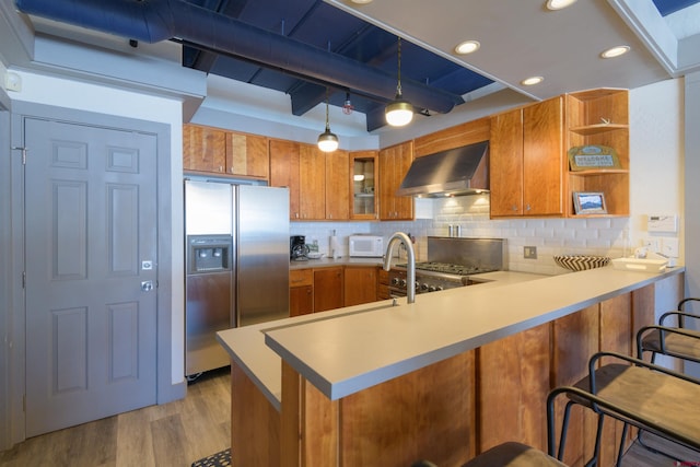 kitchen featuring wall chimney range hood, stainless steel refrigerator with ice dispenser, pendant lighting, kitchen peninsula, and backsplash