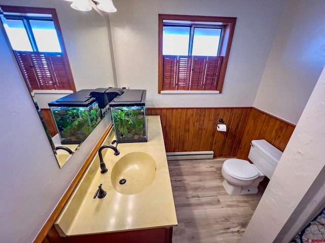 bathroom featuring hardwood / wood-style floors, wood walls, toilet, baseboard heating, and oversized vanity