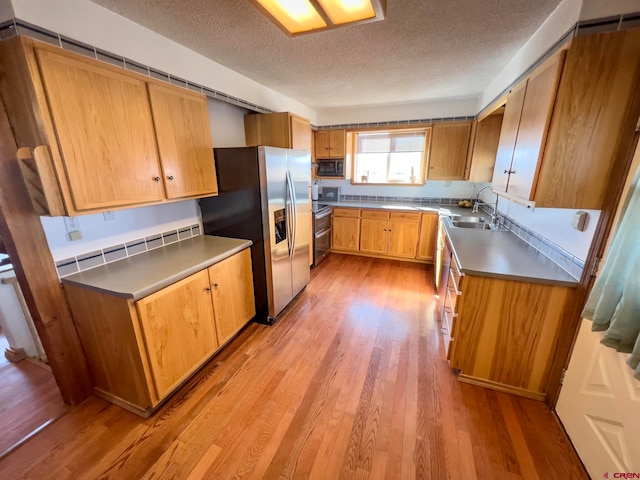 kitchen with a textured ceiling, black microwave, stainless steel fridge with ice dispenser, light hardwood / wood-style flooring, and sink