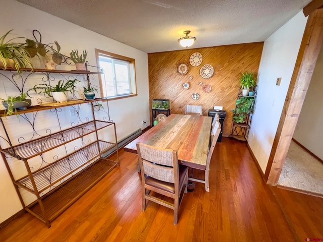 dining space featuring wooden walls, a textured ceiling, and hardwood / wood-style flooring