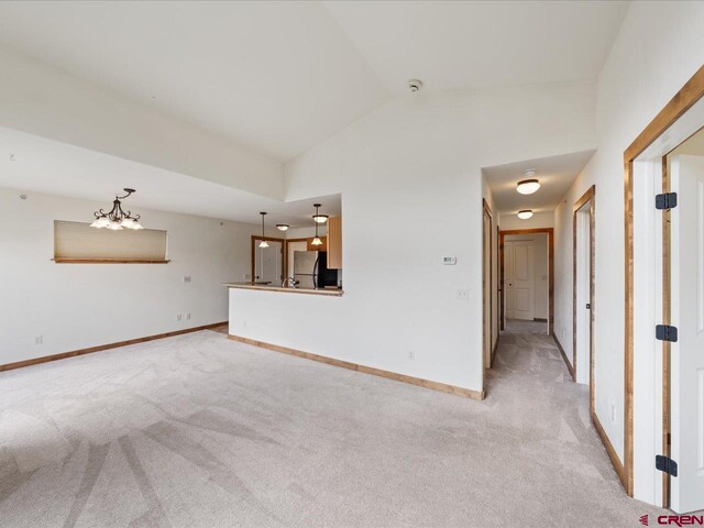 carpeted spare room with an inviting chandelier and lofted ceiling