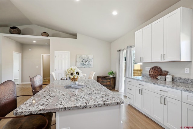 kitchen with white cabinets, a kitchen bar, light stone countertops, and a center island