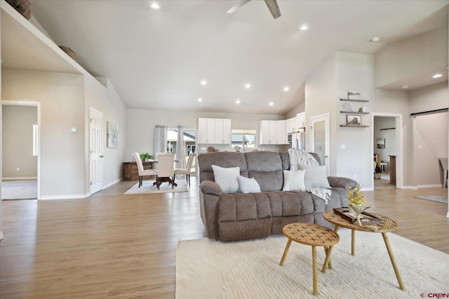 living room with ceiling fan, light wood-type flooring, and high vaulted ceiling