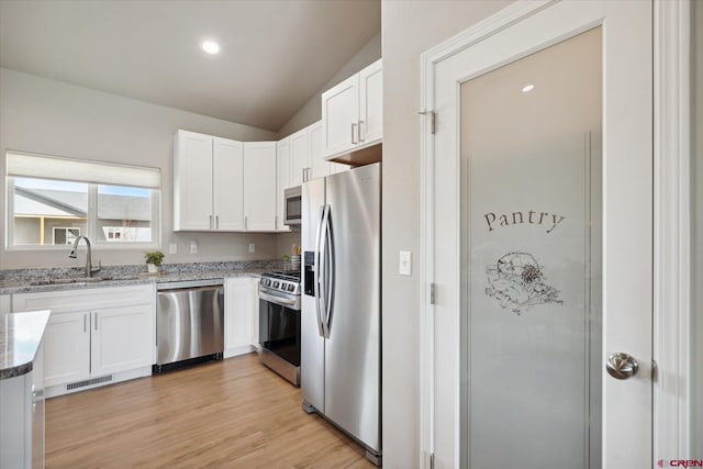 kitchen with sink, light stone counters, appliances with stainless steel finishes, vaulted ceiling, and light wood-type flooring