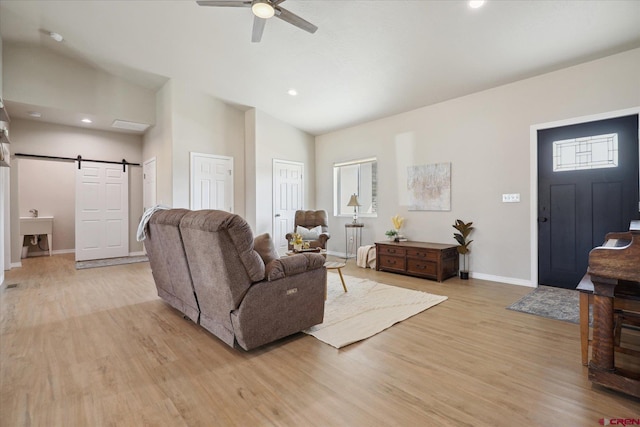 living room featuring ceiling fan, vaulted ceiling, a barn door, and light hardwood / wood-style floors