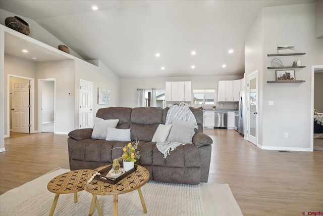 living room with high vaulted ceiling, sink, and light wood-type flooring