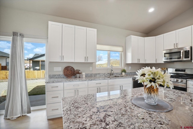 kitchen with white cabinets, appliances with stainless steel finishes, light stone counters, and sink