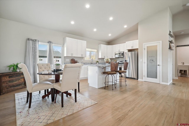 dining space featuring high vaulted ceiling, light hardwood / wood-style floors, and sink