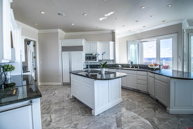 kitchen with dark stone countertops, white cabinetry, light tile flooring, and an island with sink