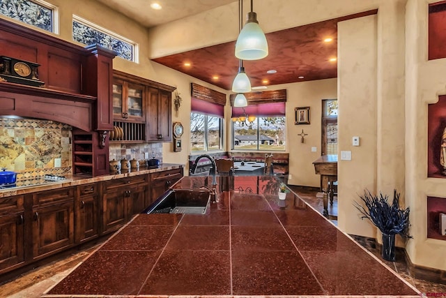 interior space with hanging light fixtures, stainless steel gas cooktop, backsplash, sink, and premium range hood