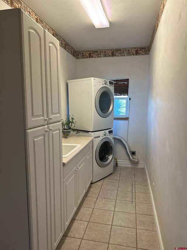 laundry area with stacked washer / dryer, sink, cabinets, and light tile flooring