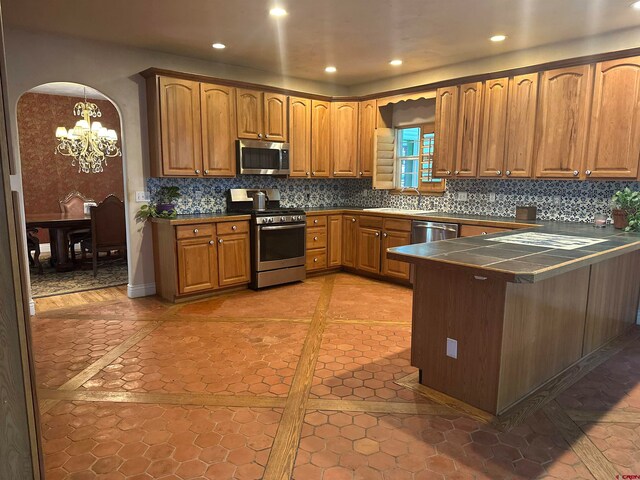 kitchen featuring hanging light fixtures, backsplash, appliances with stainless steel finishes, a notable chandelier, and light tile floors