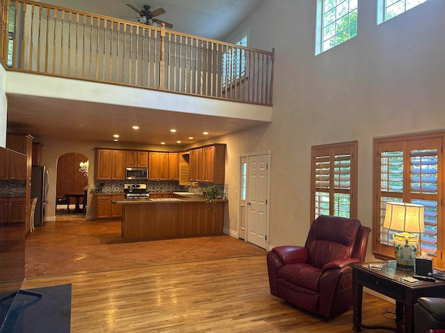 living room with ceiling fan, a towering ceiling, and light wood-type flooring