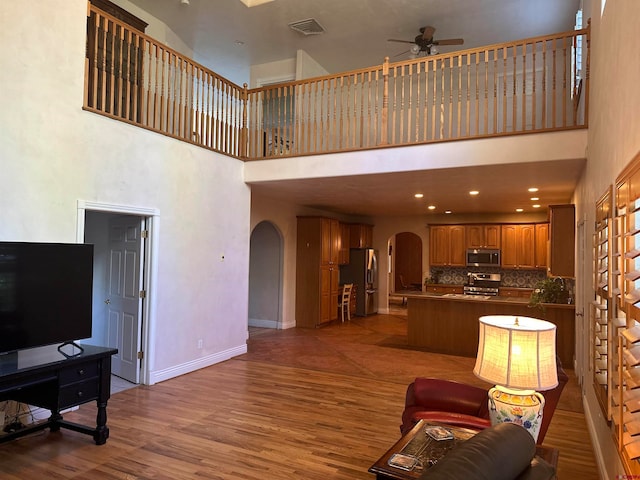 living room featuring wood-type flooring, ceiling fan, and a towering ceiling