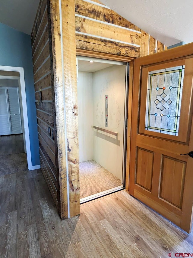 entryway with vaulted ceiling, elevator, and wood-type flooring