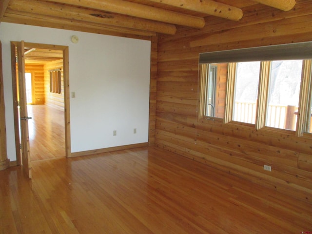 spare room featuring beam ceiling, light hardwood / wood-style floors, and log walls