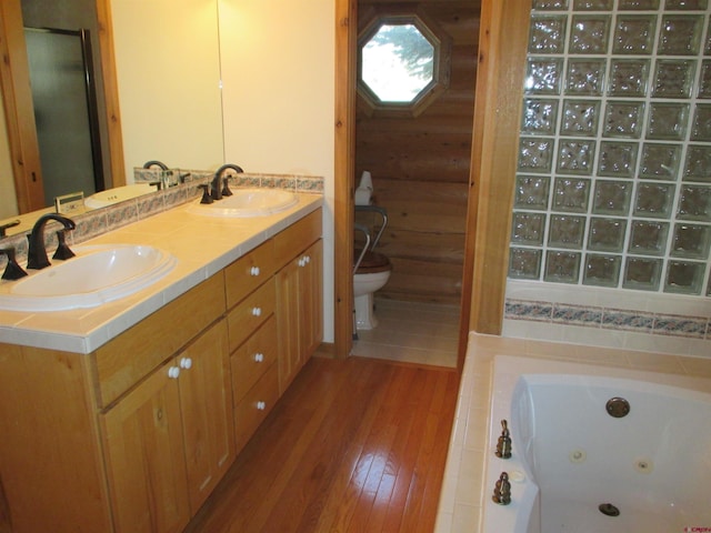 bathroom with wood-type flooring, large vanity, dual sinks, toilet, and a washtub