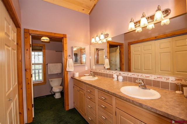 bathroom with lofted ceiling, backsplash, toilet, and dual bowl vanity