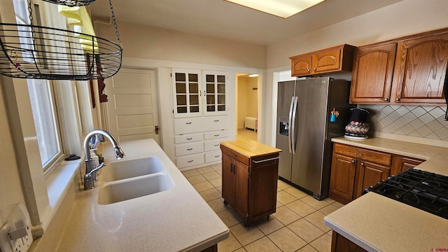 kitchen with a center island, sink, stainless steel fridge, light tile patterned flooring, and tasteful backsplash