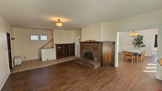 living room featuring light hardwood / wood-style flooring, radiator heating unit, a notable chandelier, and a brick fireplace