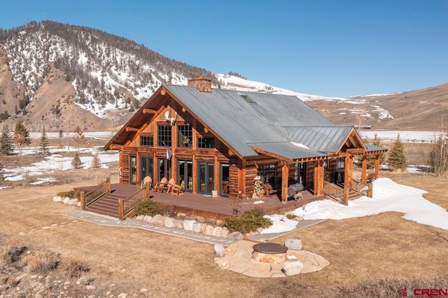 snow covered back of property with a fire pit and a deck with mountain view