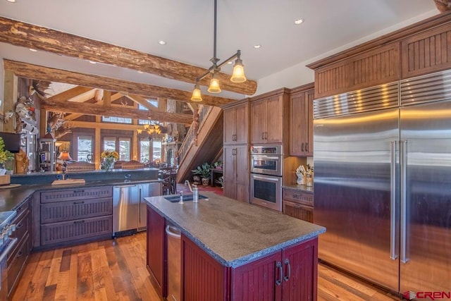 kitchen featuring sink, an island with sink, appliances with stainless steel finishes, beamed ceiling, and decorative light fixtures