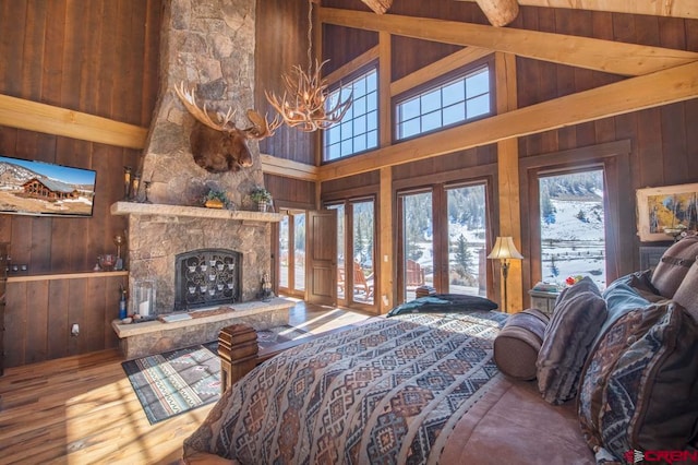 bedroom with an inviting chandelier, high vaulted ceiling, wood walls, hardwood / wood-style floors, and a fireplace