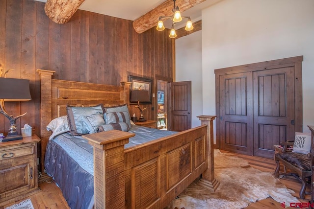 bedroom with beamed ceiling, light hardwood / wood-style floors, an inviting chandelier, and wooden walls