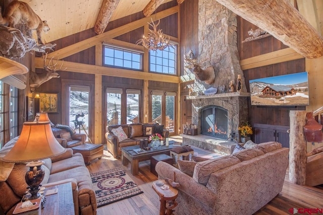 living room with beam ceiling, high vaulted ceiling, an inviting chandelier, hardwood / wood-style floors, and a stone fireplace