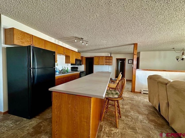 kitchen with a center island, a breakfast bar, a baseboard radiator, black appliances, and a textured ceiling