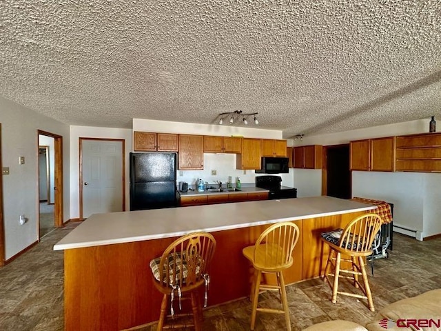 kitchen featuring a baseboard heating unit, black appliances, rail lighting, sink, and a breakfast bar area