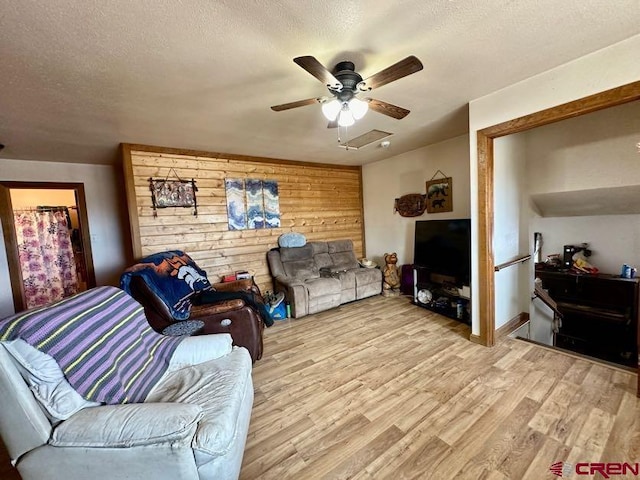 living room with wooden walls, ceiling fan, a textured ceiling, and light wood-type flooring